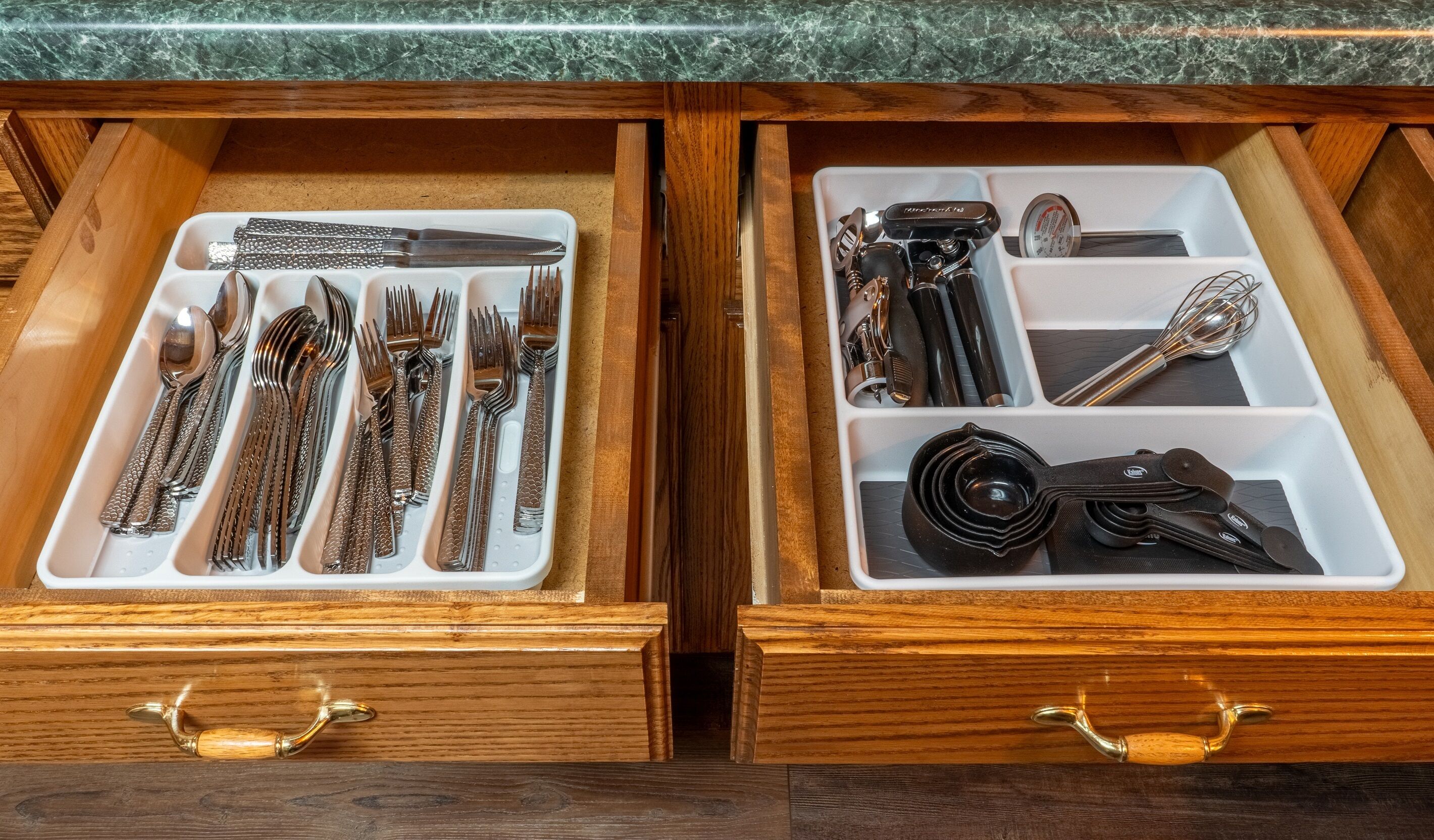 Dos cajones de madera con divisiones que contienen cubiertos y utensilios de cocina.