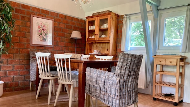 A dining area with a brick wall, wooden furniture, and a window with curtains. - Holiday House Viktoria at Lake Lauwersmeer (Anjum)