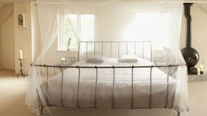 A bedroom with a four-poster bed, a large window, a fireplace, and a bedside table with a candle. - Patricius Haus Comfortable Holiday Residence (Oostwoud)