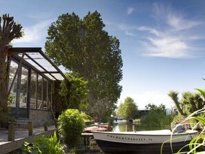 A boat docked at a canal with a glass structure nearby. - Patricius Haus Comfortable Holiday Residence (Oostwoud)