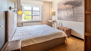 A bedroom with a bed, a window, a painting, a bedside table, and a radiator. - Apartment in Koksijde With Terrace & Garden (Koksijde)