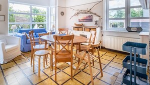 A bright, open-plan living and dining area with a large window, a dining table, and blue furniture. - Apartment in Koksijde With Terrace & Garden (Koksijde)