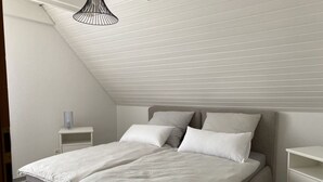Ett sovrum med ett sluttande tak, en säng med två kuddar, ett sängbord och en lampa.