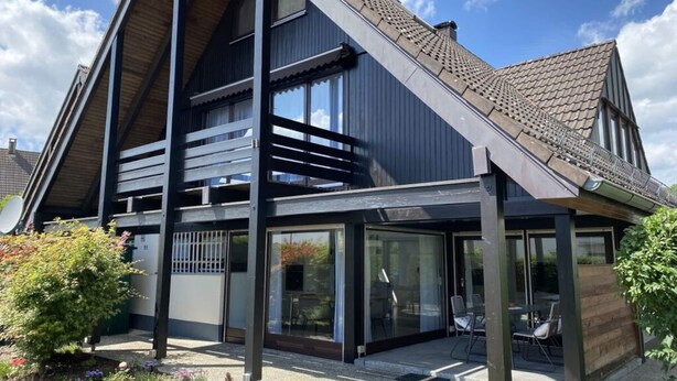 Ett modernt hus i två våningar med ett sluttande tak, stora fönster och en täckt uteplats.