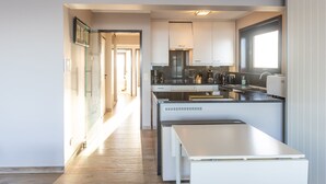 A modern kitchen with white cabinets, a built-in oven, and a window providing natural light. - Corner Apartment With Frontal sea View (Middelkerke)
