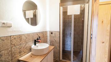 A bathroom with a round mirror, a sink with a wooden countertop, patterned tiles, and a shower area with a glass door.