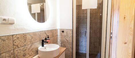 A bathroom with a round mirror, a sink with a wooden countertop, patterned tiles, and a shower area with a glass door.