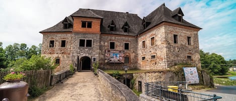 A historic stone building with a central entrance, a covered walkway, and a signboard.