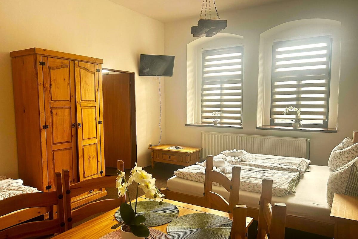 Una habitación acogedora con un armario de madera, una mesa de comedor con sillas, una mesita de noche pequeña y una cama con ropa de cama estampada.