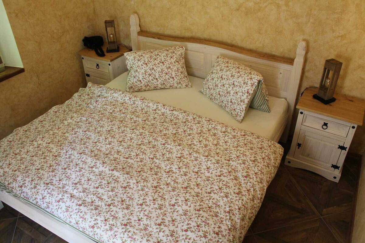 Un dormitorio con colcha estampada, dos almohadas, cabecera de madera y dos mesitas de noche con lámparas.