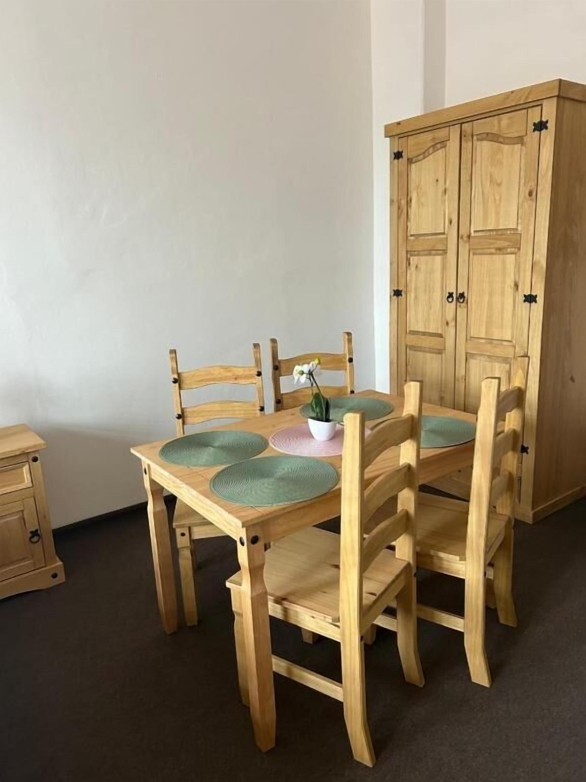 Een houten eettafel met vier stoelen, een plant in pot en een kast op de achtergrond.