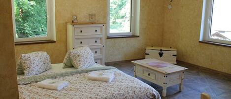 A bedroom with a bed, dresser, nightstand, and a window with a view of trees.
