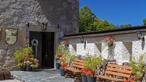Un edificio rústico de piedra con puerta de madera, bancos exteriores y plantas en macetas.