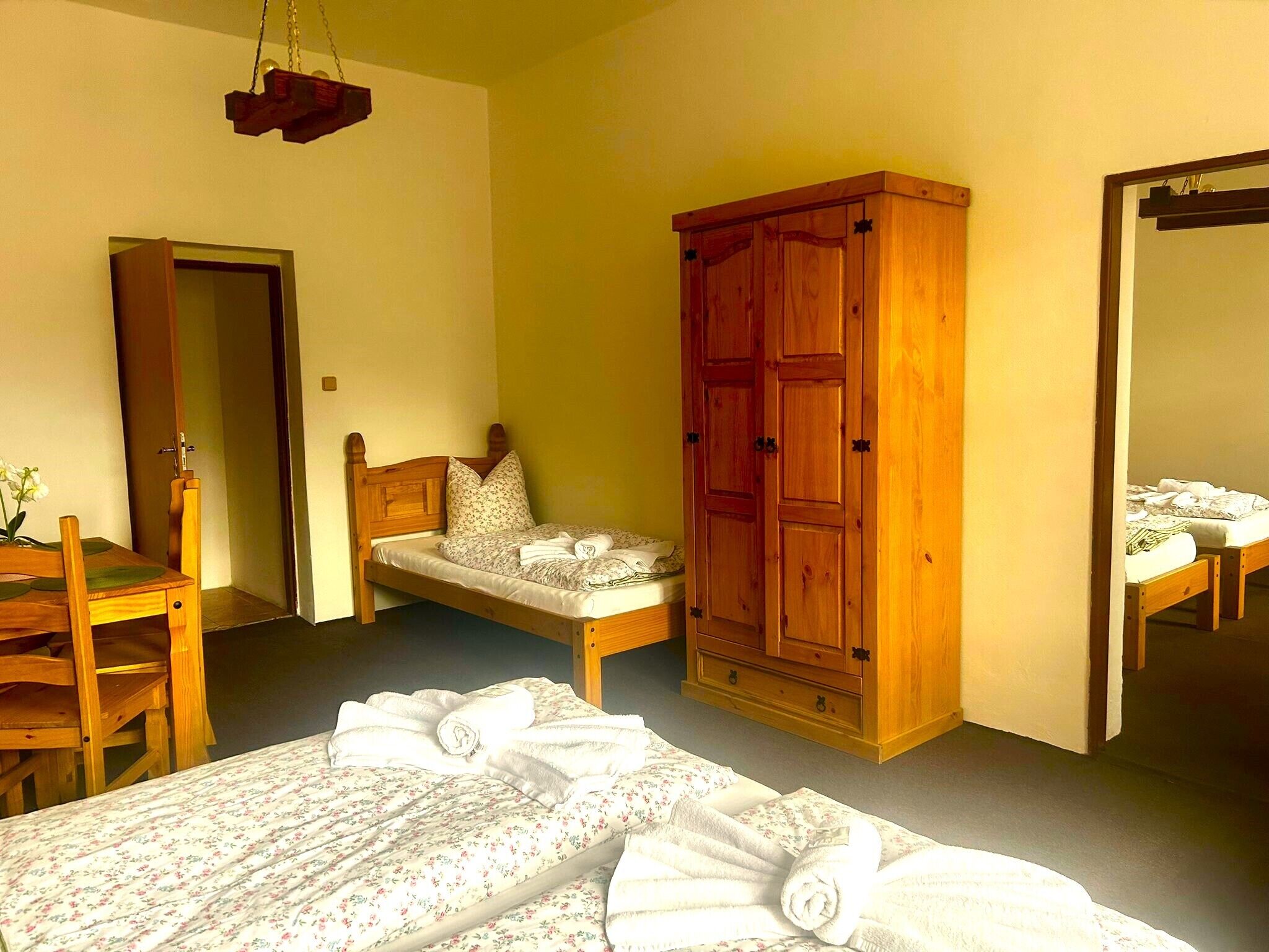 A bedroom with two single beds, a wooden wardrobe, a wooden chair, and a small table with a vase of flowers.