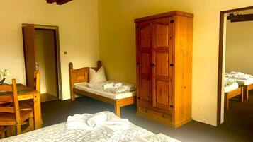 A bedroom with two single beds, a wooden wardrobe, a wooden chair, and a small table with a vase of flowers.