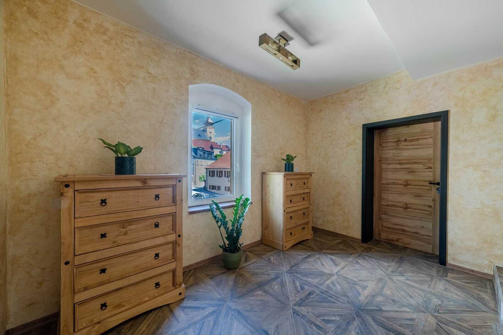 A room with a large window, wooden cabinets, a potted plant, and a door.