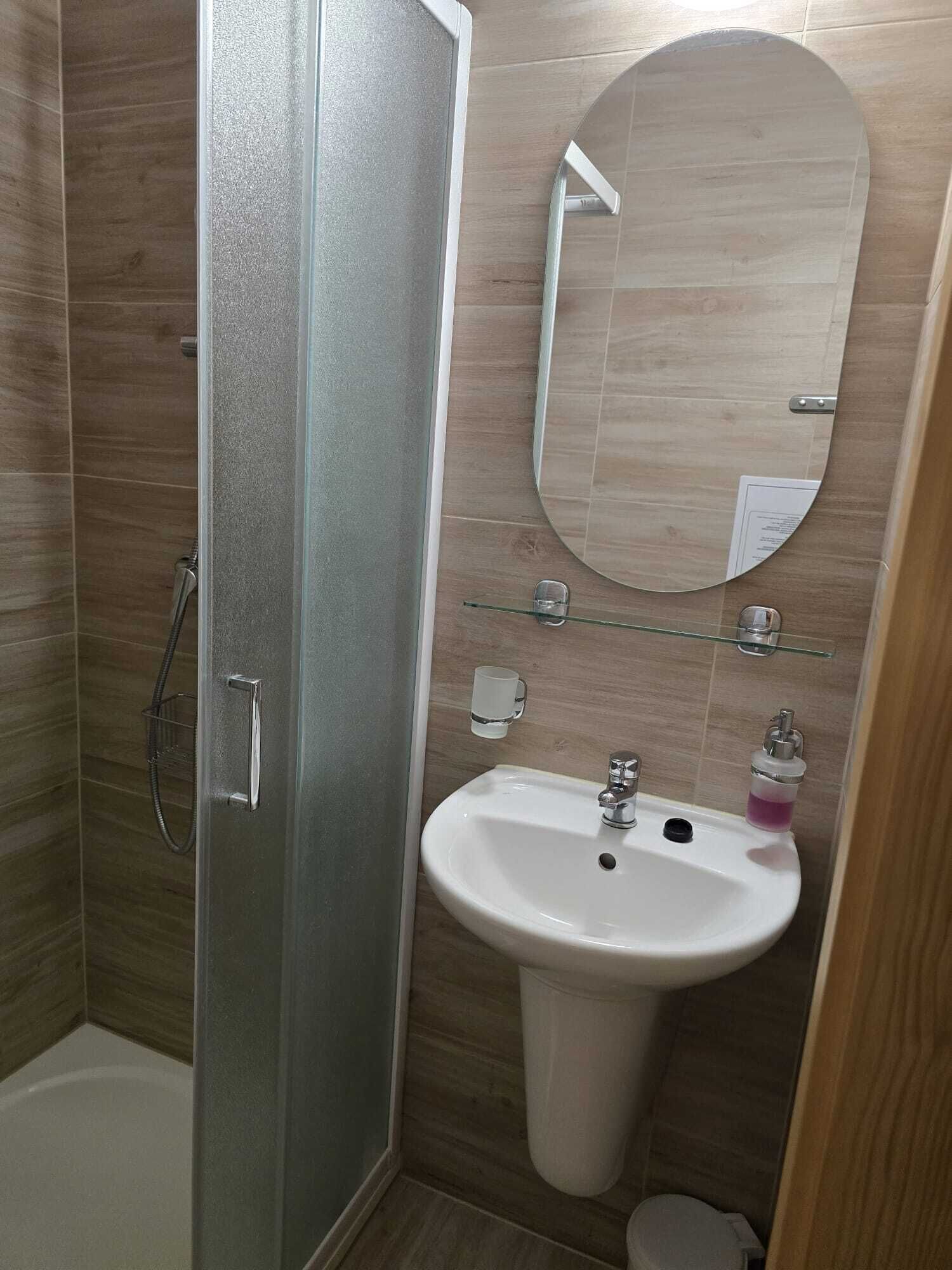 A bathroom with a glass shower enclosure, a white sink with a mirror above it, and a small shelf with toiletries.