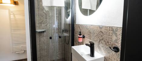 A modern bathroom with a glass shower enclosure, a white sink, and a mirror with a round frame.