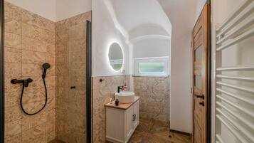 Een badkamer met een douche, een wastafel met spiegel en een raam.