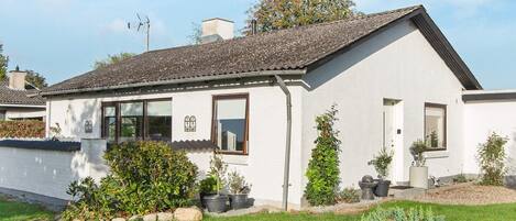 A single-story house with a white exterior, a tiled roof, and a front yard with potted plants and a well-maintained lawn.