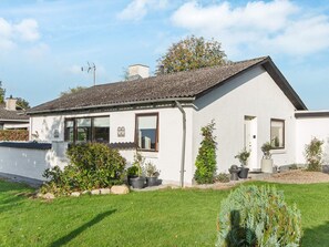 Uma casa térrea com fachada branca, telhado telhado e um jardim frontal com vasos de plantas e gramado bem cuidado.