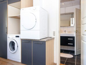 A laundry area with a front-loading washing machine and a dryer, a sink with a mirror, and a door leading to a bathroom. - 4 Person Holiday Home in Haderslev (Haderslev)