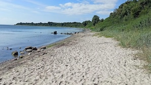 A sandy beach with rocks, a clear sky, and a distant forested area. - 4 Person Holiday Home in Haderslev (Haderslev)