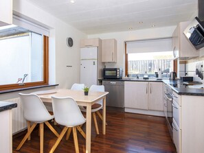 Cozinha moderna com área de refeições, piso de madeira e vista pela janela.
