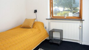 A single bed with a yellow quilt, a small bedside table, a radiator, and a window with a view of the outside. - 4 Person Holiday Home in Haderslev (Haderslev)