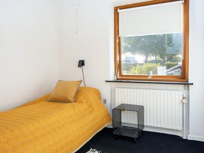 A single bed with a yellow quilt, a small bedside table, a radiator, and a window with a view of the outside. - 4 Person Holiday Home in Haderslev (Haderslev)