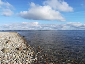 A pebbly beach with clear water and distant land under a partly cloudy sky. - 4 Person Holiday Home in Haderslev (Haderslev)
