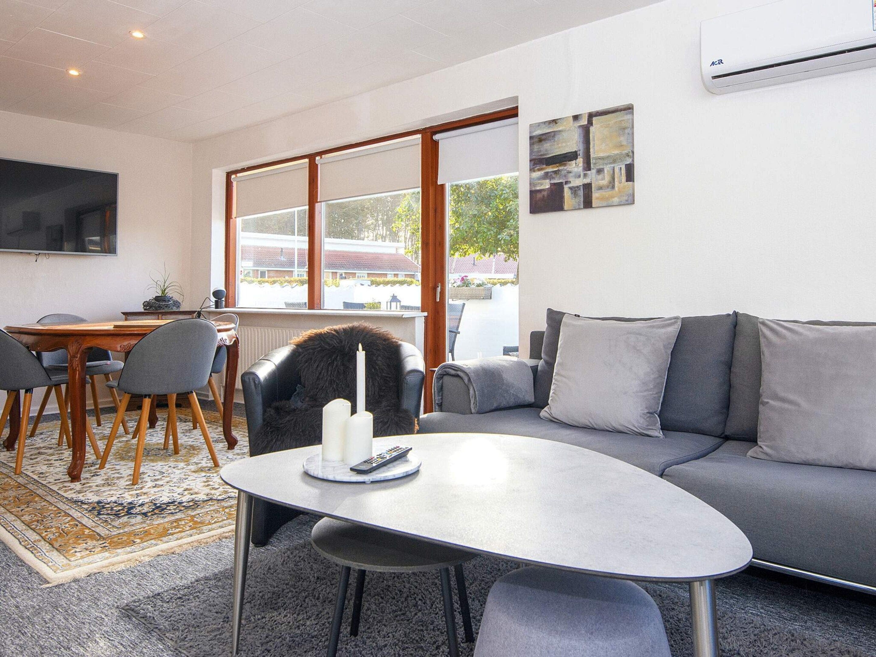 A modern living room with a grey sofa, a round coffee table, and a dining area with a wooden table and chairs.