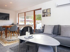 A modern living room with a grey sofa, a round coffee table, and a dining area with a wooden table and chairs. - 4 Person Holiday Home in Haderslev (Haderslev)