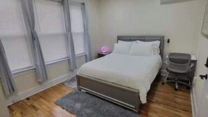 Una camera da letto con pavimento in legno, un letto con biancheria bianca, una scrivania e una sedia.
