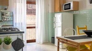 A compact kitchen with a stove, microwave, and refrigerator. There is a dining table with chairs and a window with curtains. - In the heart of Pescara, Hope will be your home just 5 minutes from the sea. (Pescara)