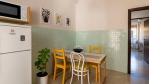 A compact kitchen with a microwave, a refrigerator, and a dining table with chairs. There are framed pictures on the wall and a potted plant on the floor. - In the heart of Pescara, Hope will be your home just 5 minutes from the sea. (Pescara)