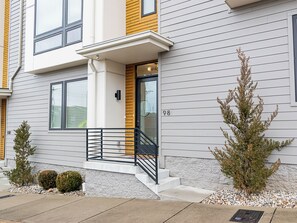 A modern two-story house with a white exterior, a wooden accent wall, and a black metal staircase leading to the entrance. - Private Rooftop Deck+ Easy walk to restaurants, music venues, and shops. (Nashville)