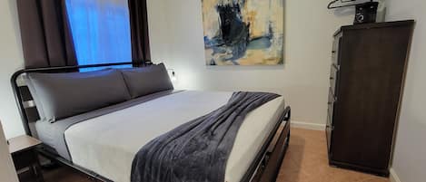 Un dormitorio ordenado con cama, armario y un cuadro en la pared.