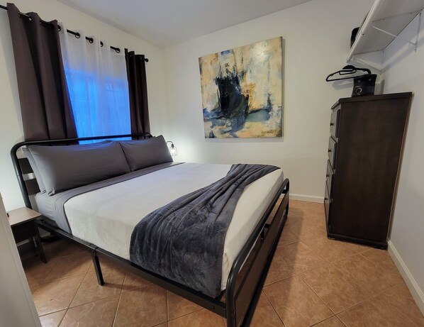 A neatly arranged bedroom with a bed, a wardrobe, and a painting on the wall.