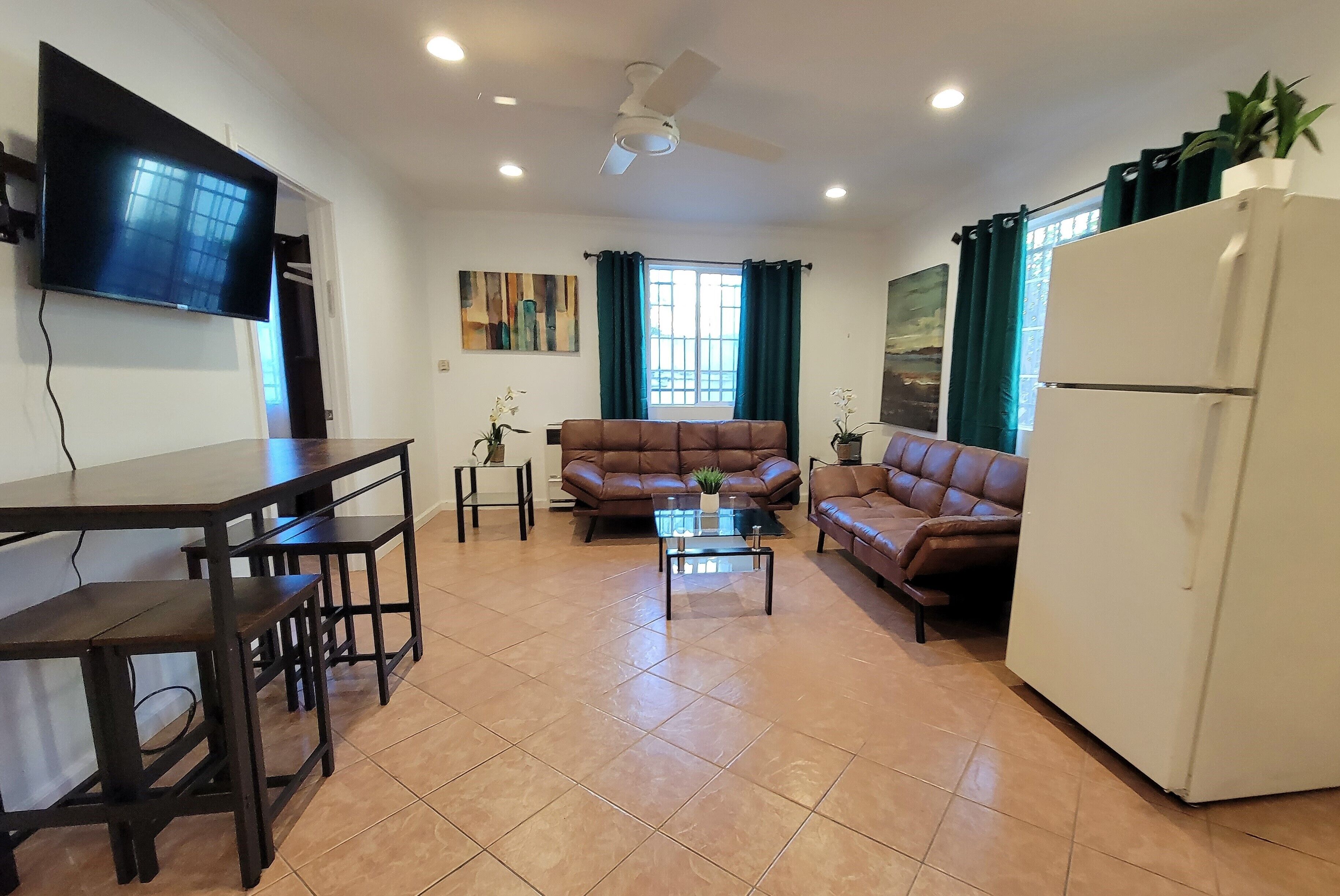 A living room with a TV, two sofas, a coffee table, a dining table, and a refrigerator.