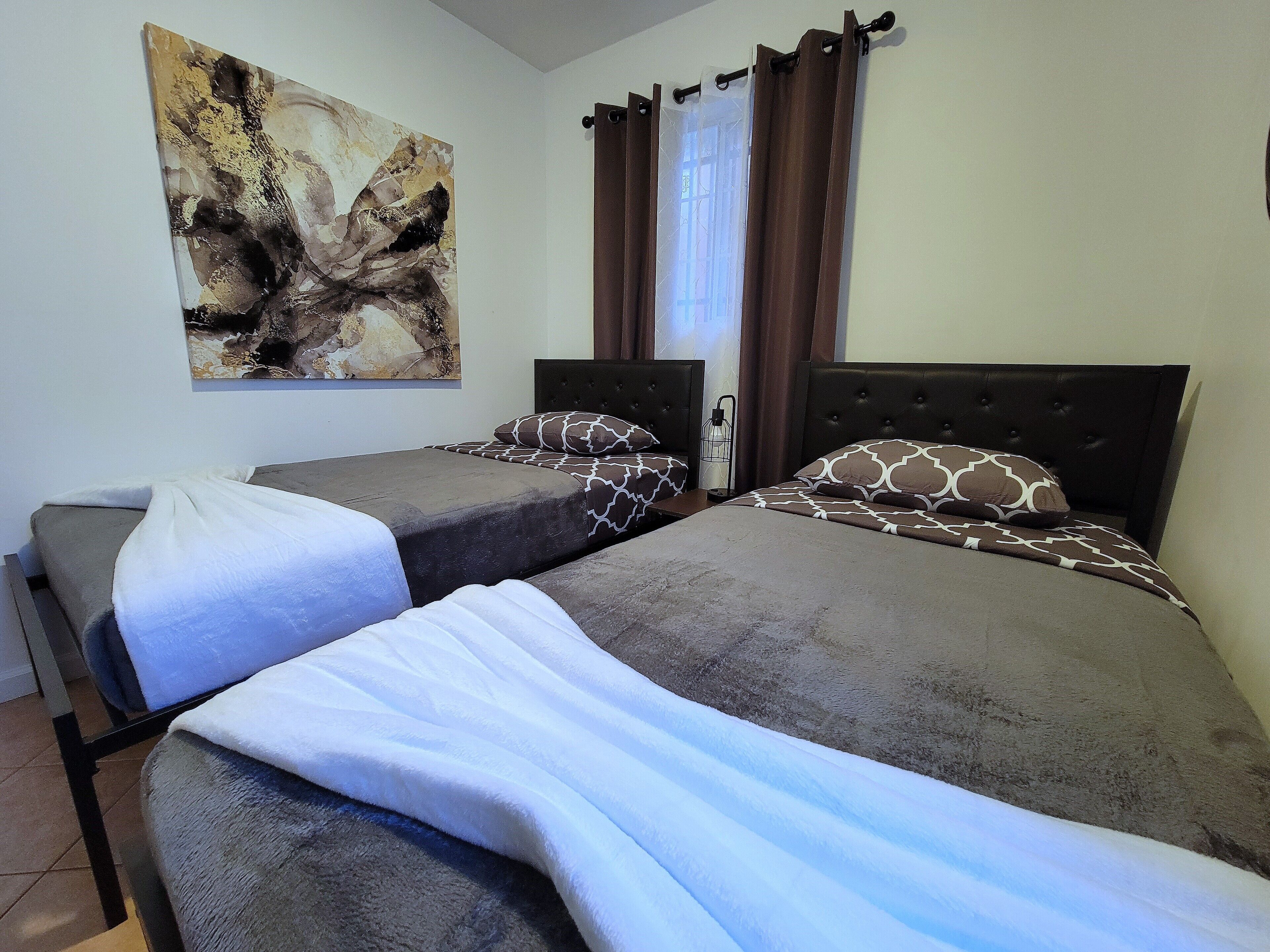 Une chambre d’hôtel avec deux lits, un grand tableau abstrait accroché au mur et une fenêtre avec des rideaux.