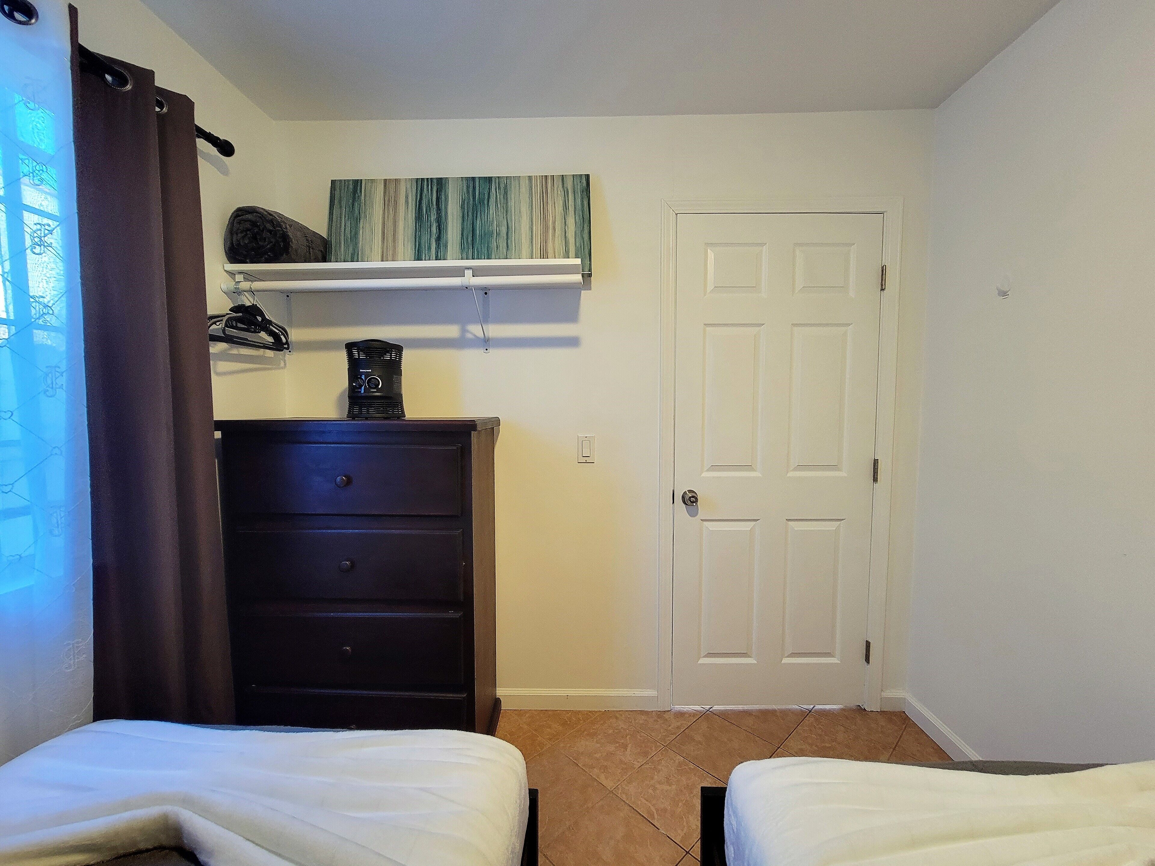 Een slaapkamer met twee bedden, een kapstok, een deur en een wandplank met een lamp.