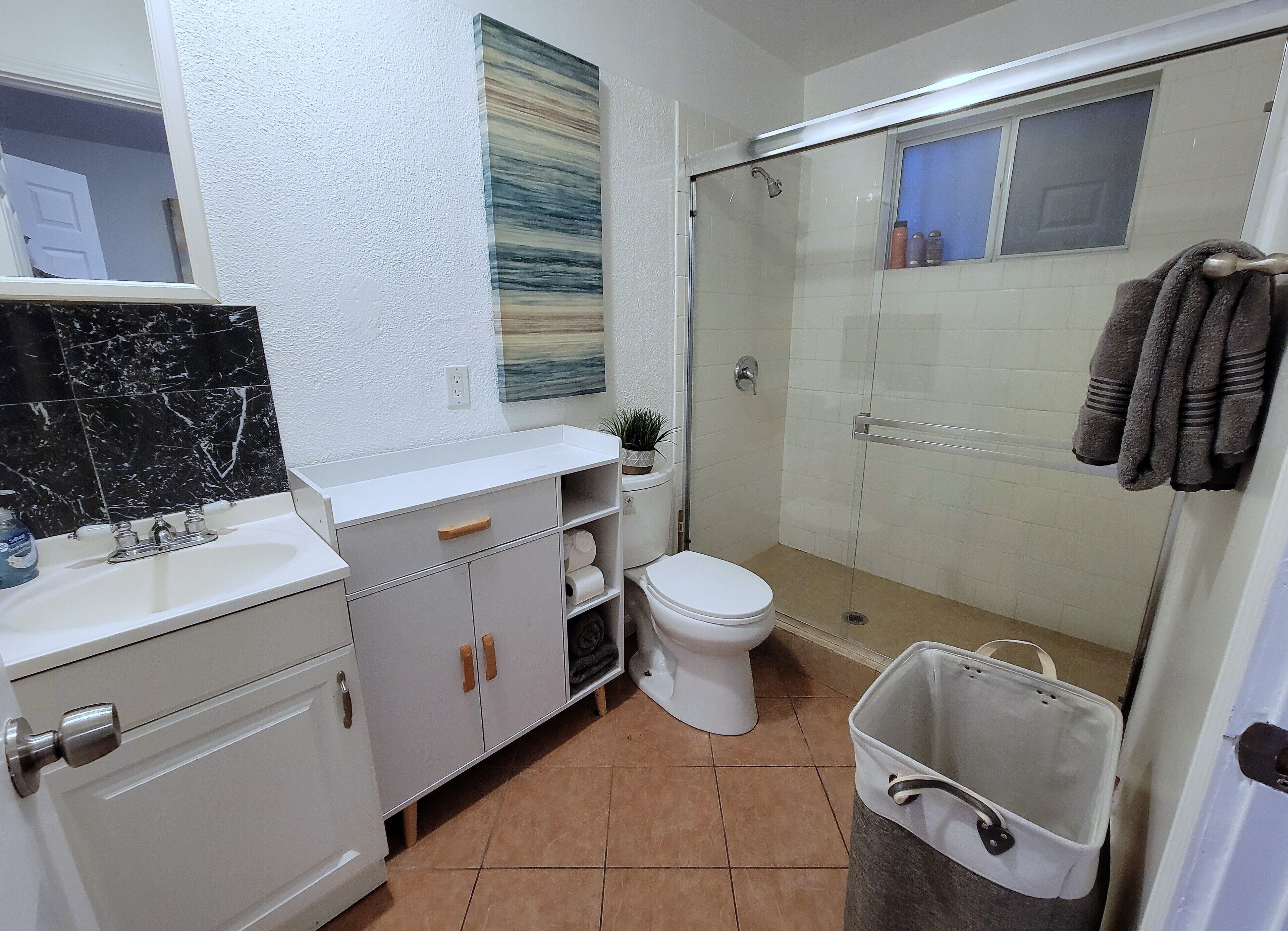 A bathroom with a white sink, a toilet, a shower, and a trash bin.