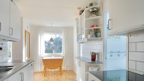 A modern kitchen with white cabinets, a wooden dining table, and a large window. - 7 Person Holiday Home in Sjaellands Odde (Sjællands Odde)