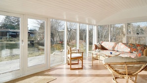 A spacious room with large glass doors leading to a garden, a wooden floor, and a wicker chair. - 7 Person Holiday Home in Sjaellands Odde (Sjællands Odde)