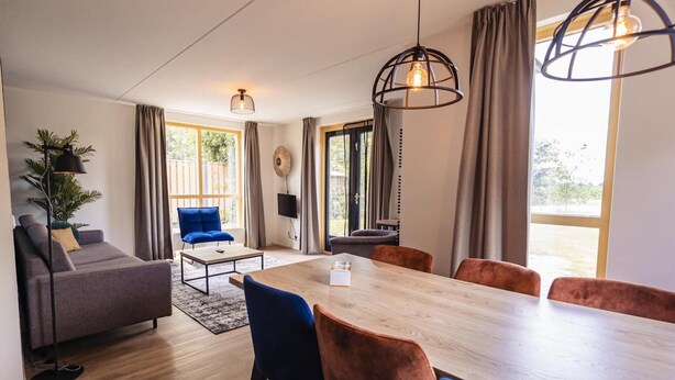 A modern living room with a sofa, a dining table with chairs, a coffee table, and a TV. - Forest Villa With Private Terrace (Ewijk)