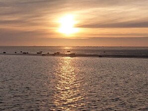 A sunset over a calm sea with boats and a distant shoreline. - West in Haus Luttmoor (Nordstrand)