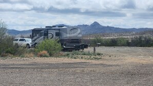 A large RV parked in a dry, rocky area with sparse vegetation and mountains in the background. - Longhorn Ranch Motel - Full Hook-Up RV Park with Power and Sewer (Alpine)