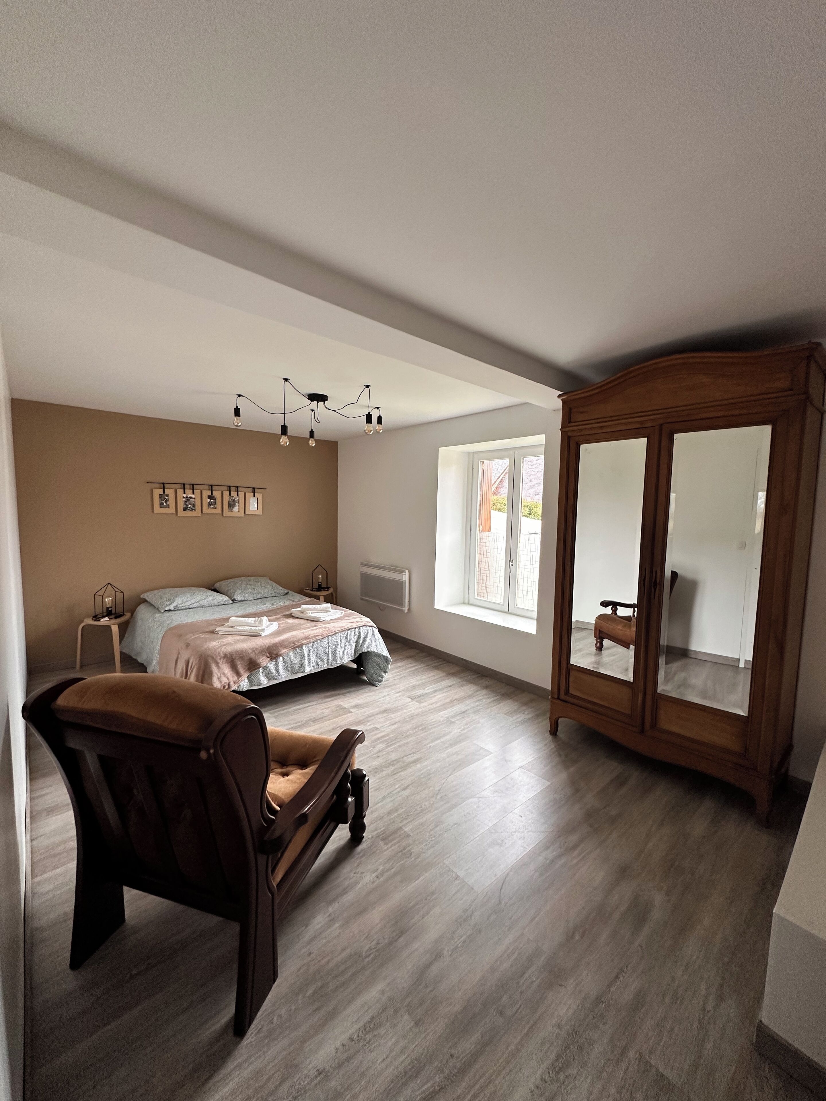 Ein Schlafzimmer mit einem Bett, einem Holzschrank, einem Stuhl, einem Nachttisch und einem Fenster.