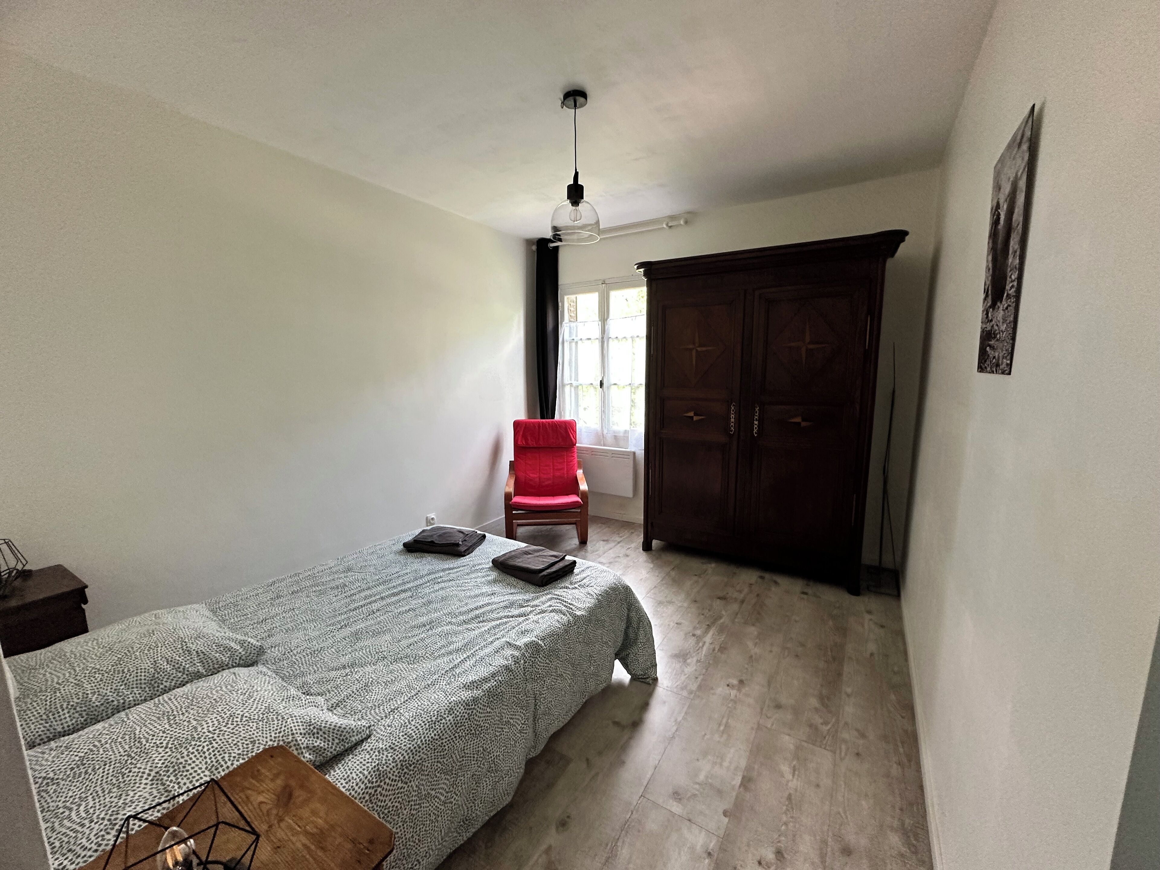 Un dormitorio con cama, una silla roja, armario y ventilador de techo.